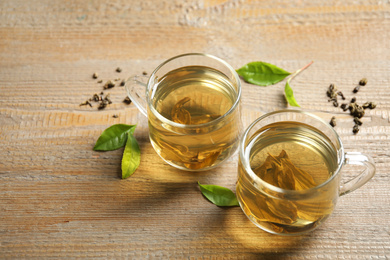 Cup of green tea, dry and fresh leaves on wooden table