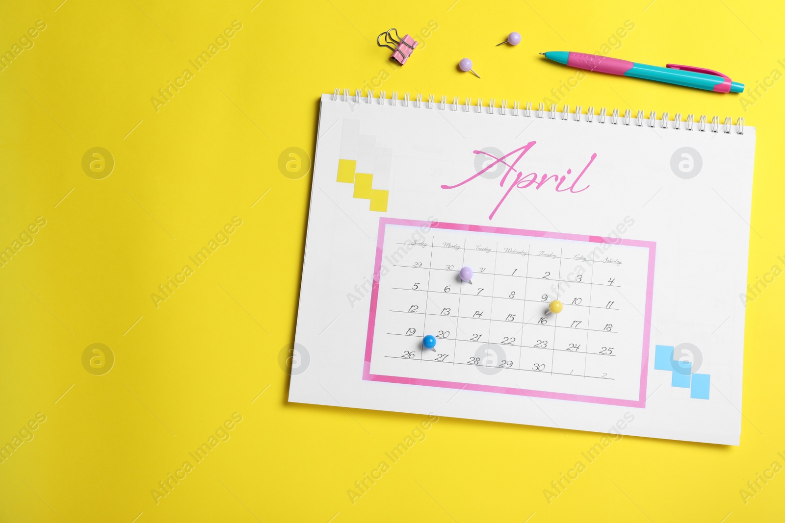 Photo of Calendar page marked with drawing pins on yellow background, flat lay