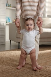Photo of Cute little baby doing first steps with mother's help at home, closeup
