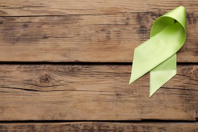 World Mental Health Day. Green ribbon on wooden background, top view with space for text