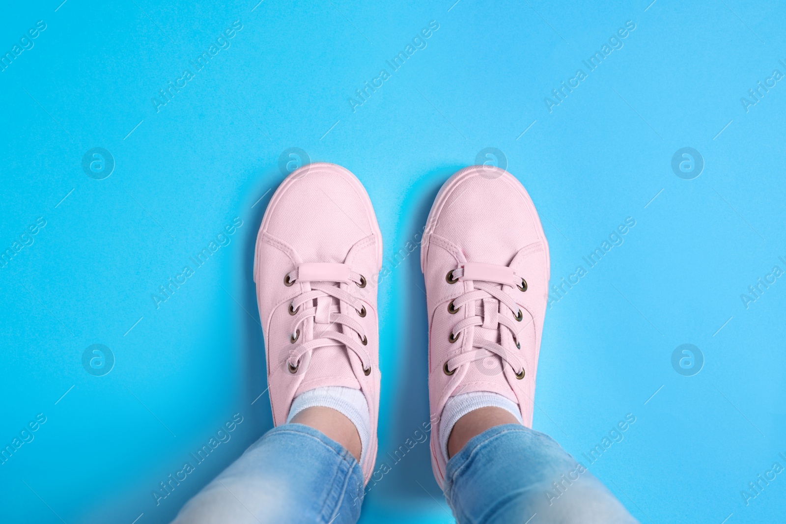 Photo of Woman in stylish sneakers standing on light blue background, top view