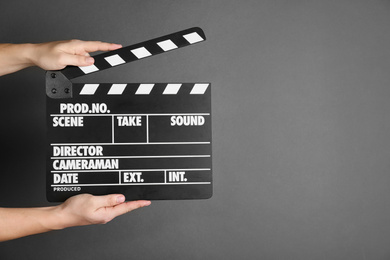 Photo of Woman holding clapperboard on dark grey background, closeup with space for text. Cinema production
