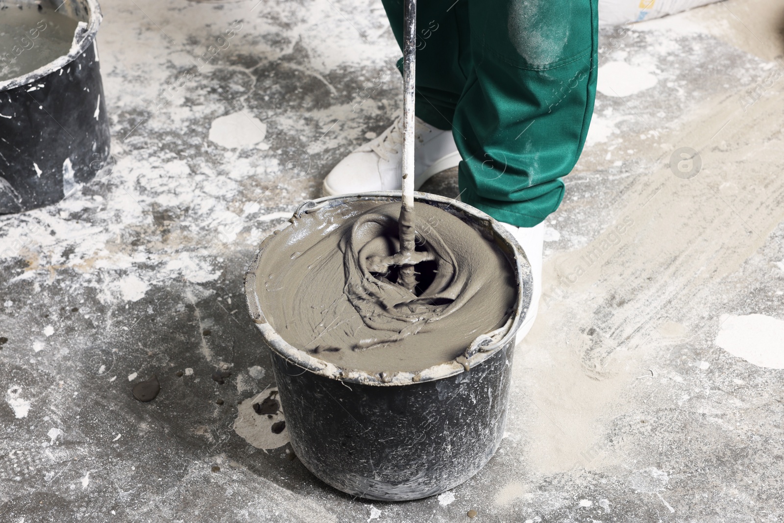 Photo of Worker mixing concrete in bucket indoors, closeup