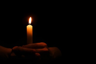 Woman holding burning candle in hands on black background, closeup. Space for text