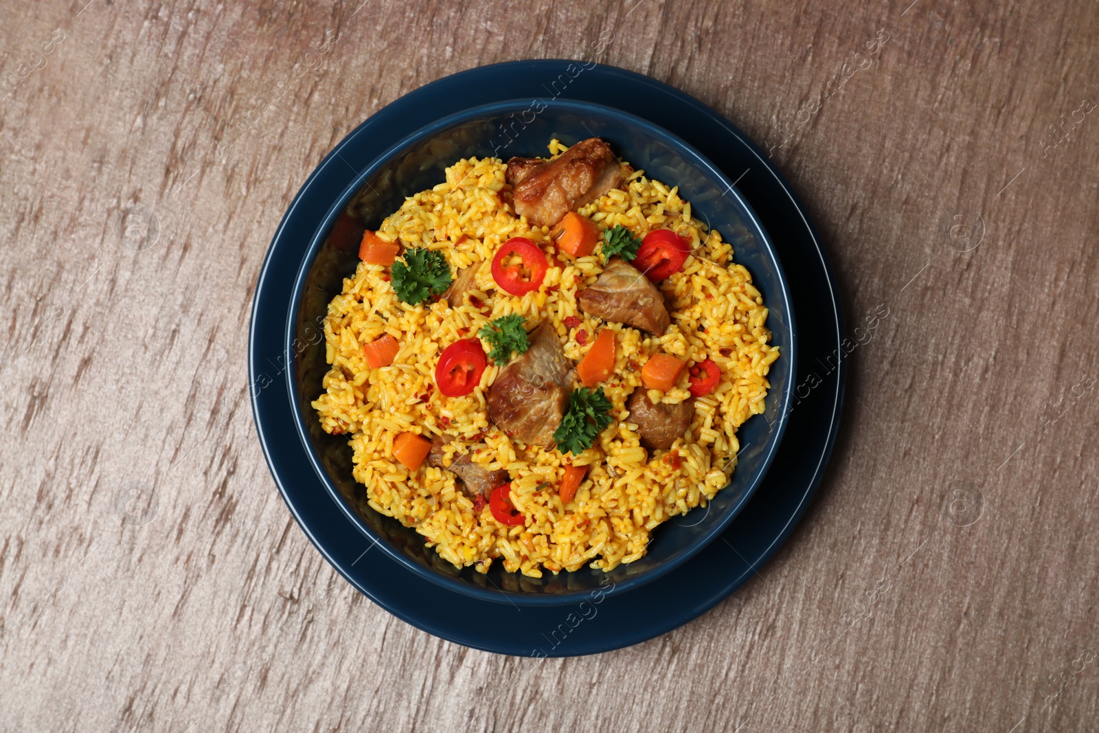 Photo of Plate with rice pilaf and meat on wooden background, top view