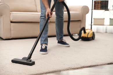 Photo of Young man using vacuum cleaner at home, closeup