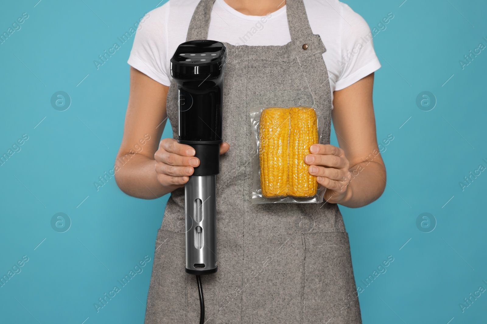 Photo of Woman holding sous vide cooker and corn in vacuum pack on light blue background, closeup