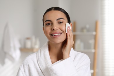 Photo of Beautiful woman removing makeup with cotton pad in bathroom