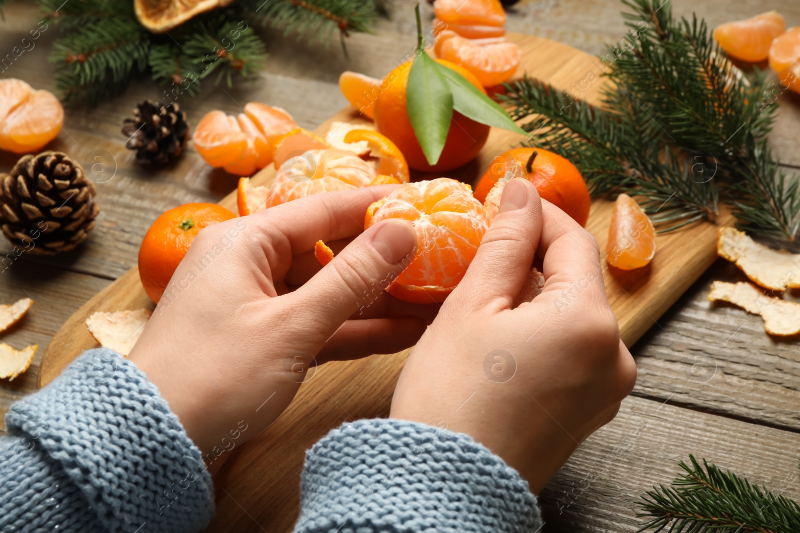 Photo of Woman peeling fresh tangerine at wooden table, closeup. Christmas atmosphere