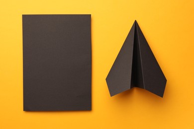Photo of Handmade black plane and piece of paper on yellow background, flat lay