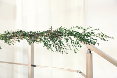 Photo of Beautiful garland made of eucalyptus branches on handrail indoors