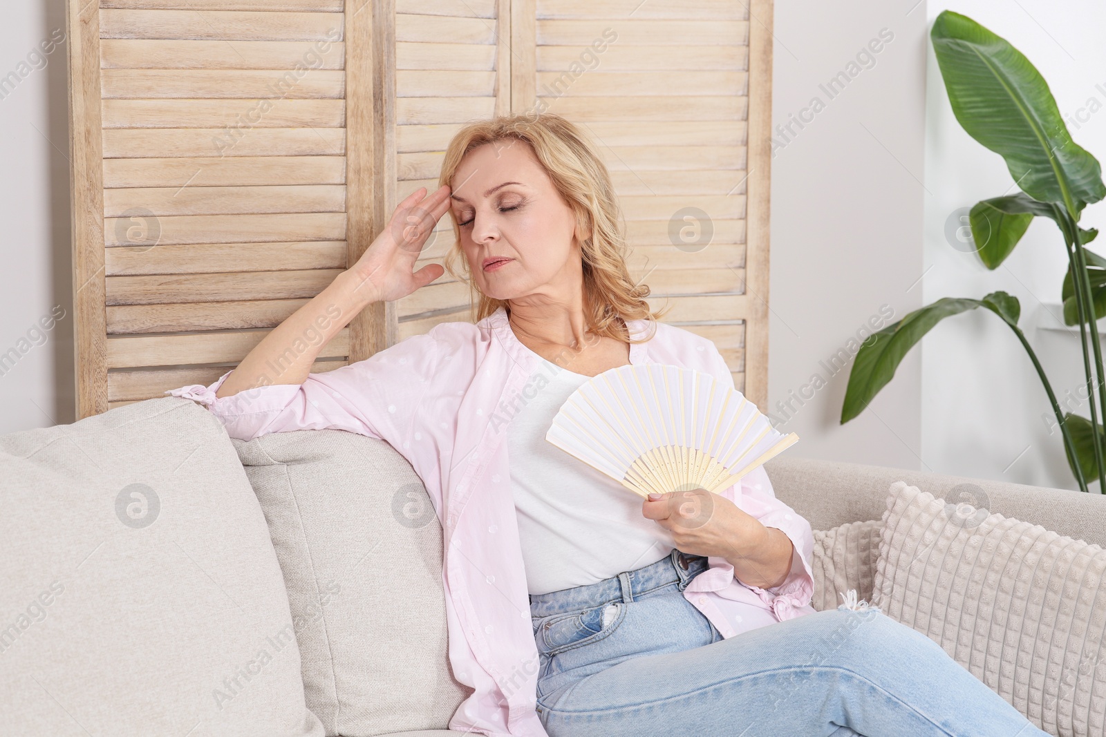 Photo of Woman waving hand fan to cool herself at home. Hormonal disorders