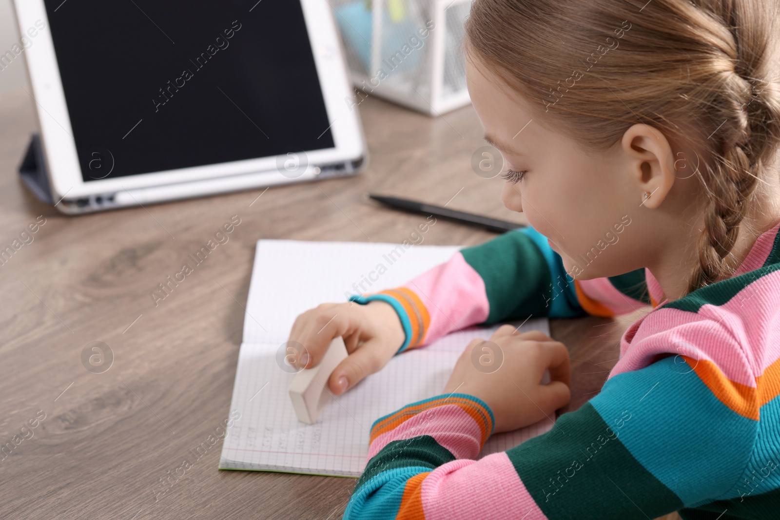 Photo of Girl erasing mistake in her homework at wooden table, closeup