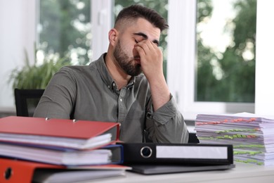 Photo of Overwhelmed man sitting at table with documents in office