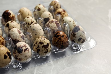 Photo of Plastic container with speckled quail eggs on light grey marble table, closeup