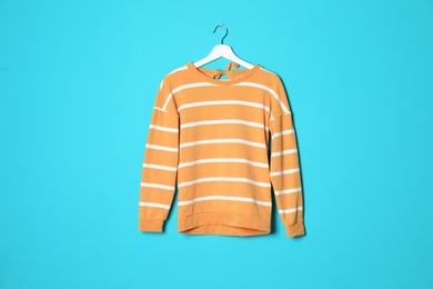 Hanger with stylish sweater on color background