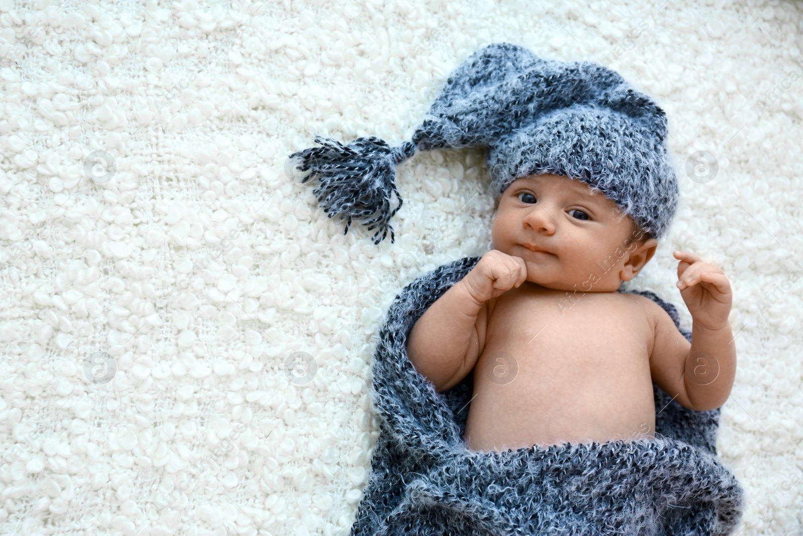Photo of Cute little baby in grey hat and plaid lying on soft blanket, top view. Space for text
