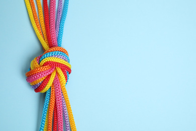 Photo of Top view of colorful ropes tied together on light blue background, space for text. Unity concept