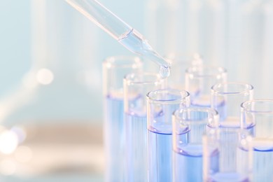 Photo of Laboratory analysis. Dripping light blue liquid from pipette into glass test tube on blurred background, closeup and space for text