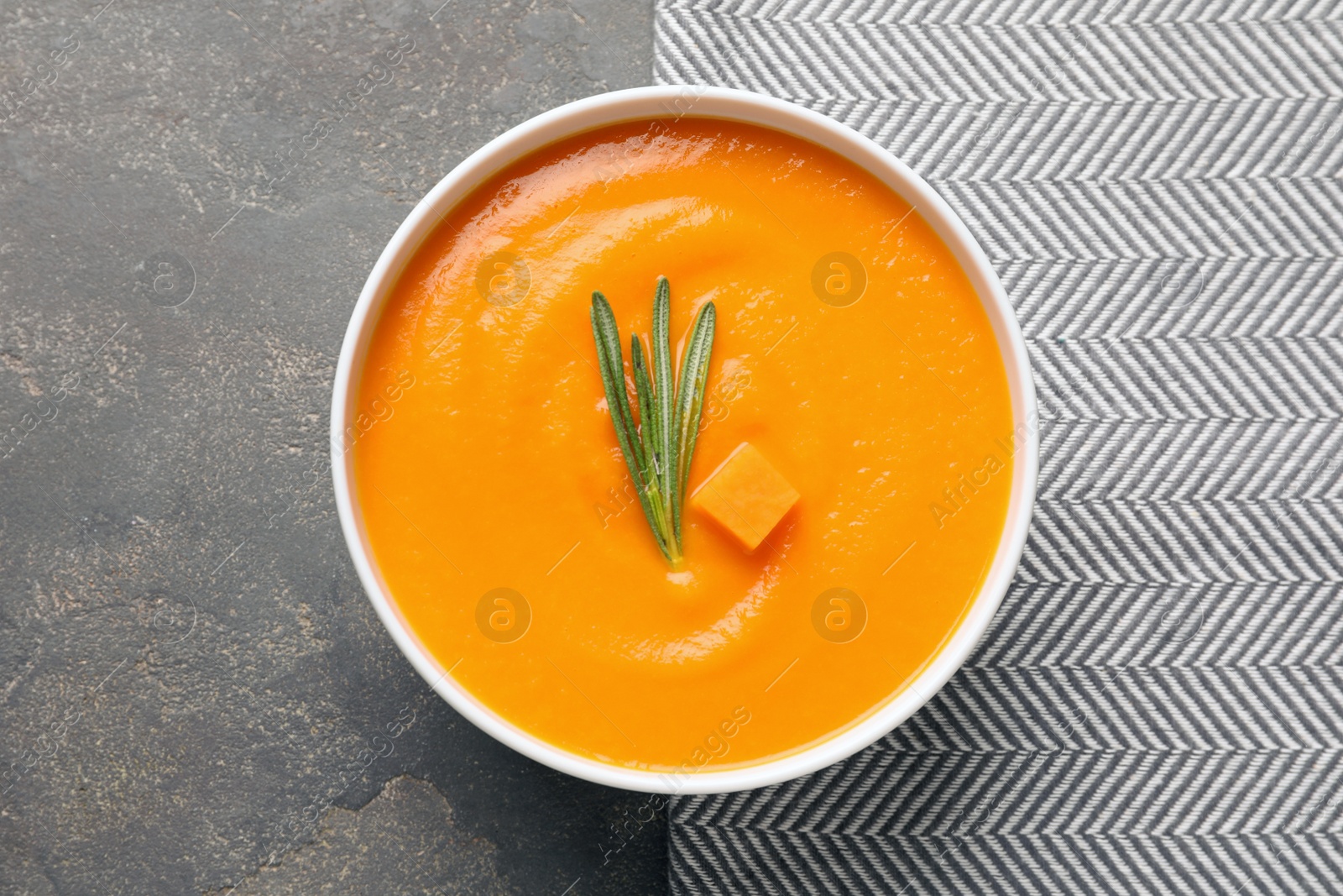 Photo of Bowl of tasty pumpkin soup on gray background, top view