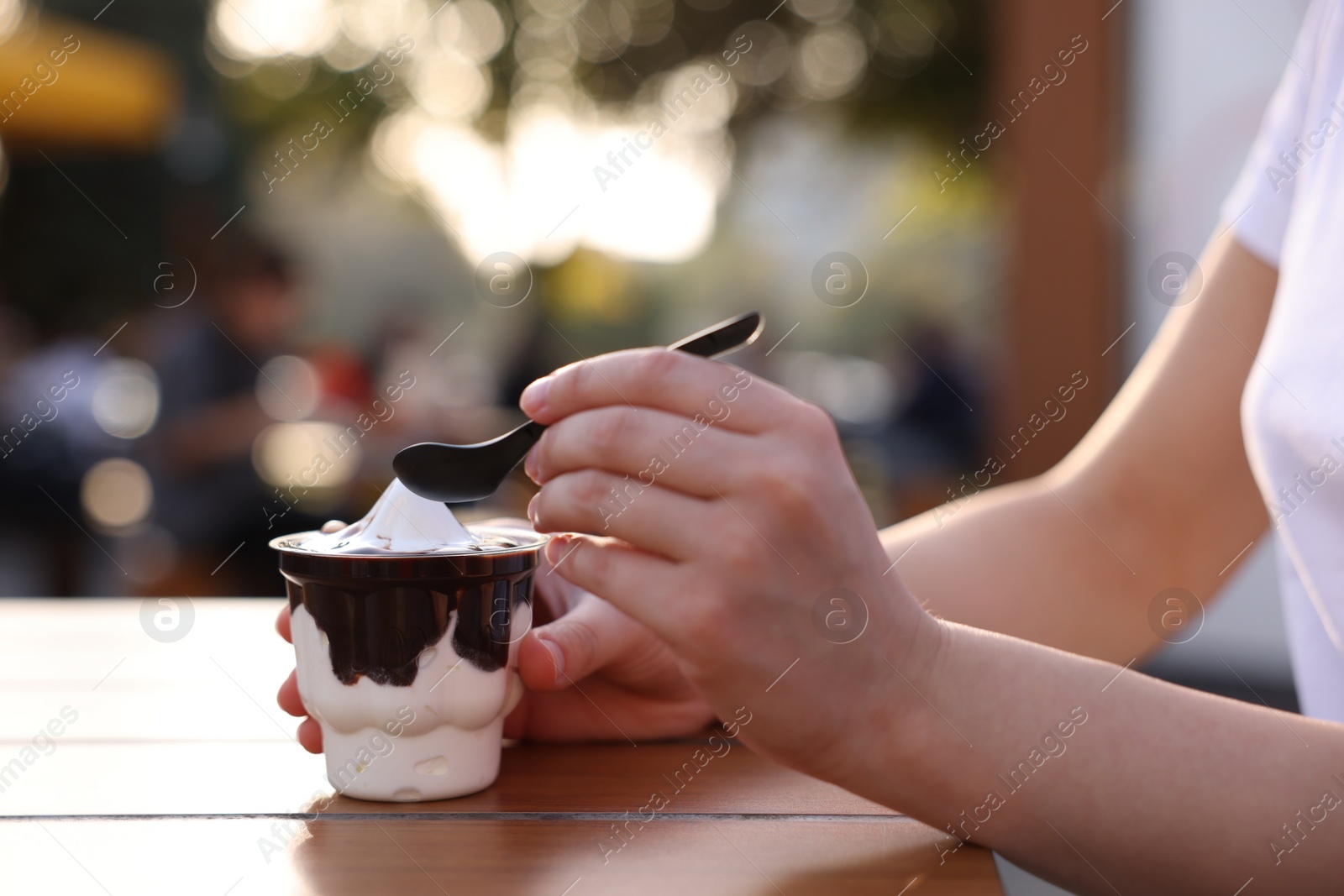 Photo of Lviv, Ukraine - September 26, 2023: Woman with McDonald's ice cream at wooden table outdoors, closeup