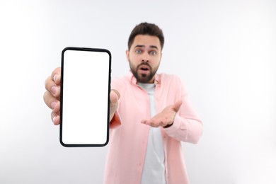 Surprised man showing smartphone in hand on white background, selective focus. Mockup for design