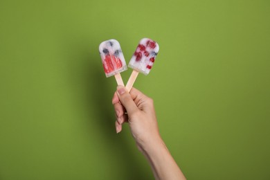 Photo of Woman holding berry popsicles on green background, closeup