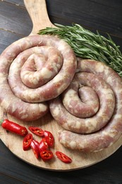 Raw homemade sausage, chili pepper and rosemary on dark wooden table, closeup