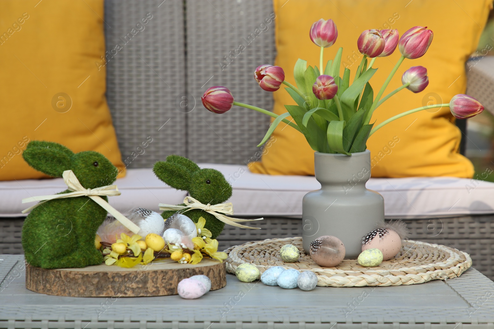 Photo of Terrace with Easter decorations. Bouquet of tulips in vase, bunny figures and decorated eggs on table outdoors