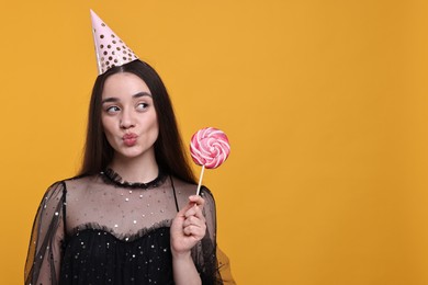 Photo of Woman in party hat holding lollipop on orange background, space for text