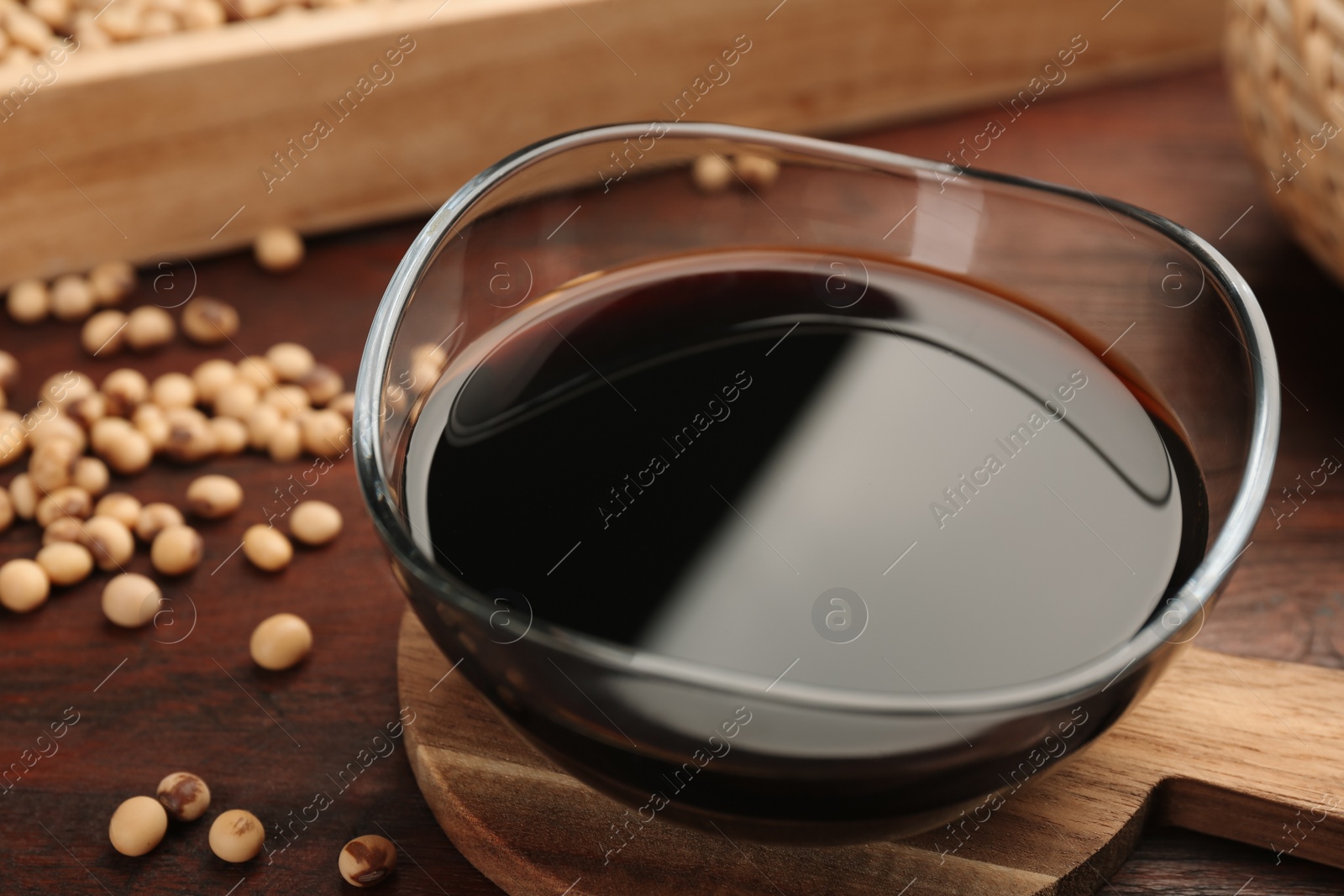 Photo of Soy sauce in bowl and soybeans on wooden table, closeup