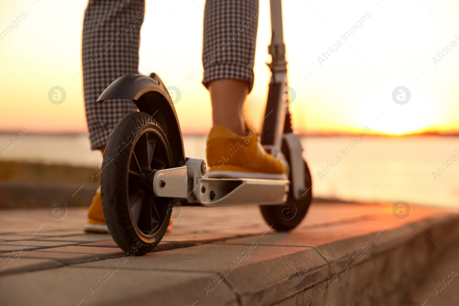 Photo of Woman riding electric kick scooter outdoors at sunset, closeup