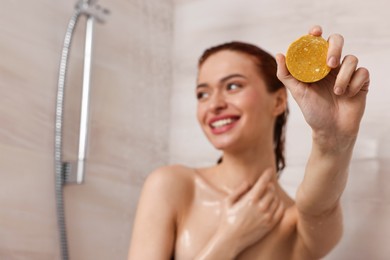 Photo of Happy young woman with solid shampoo bar in shower, selective focus. Space for text