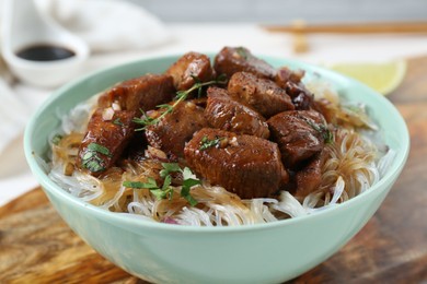 Photo of Bowl with pieces of soy sauce chicken and noodle on wooden board, closeup