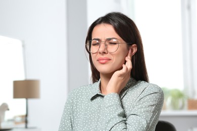 Photo of Young woman in eyeglasses suffering from ear pain indoors