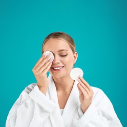 Beautiful young woman with cotton pads on turquoise background