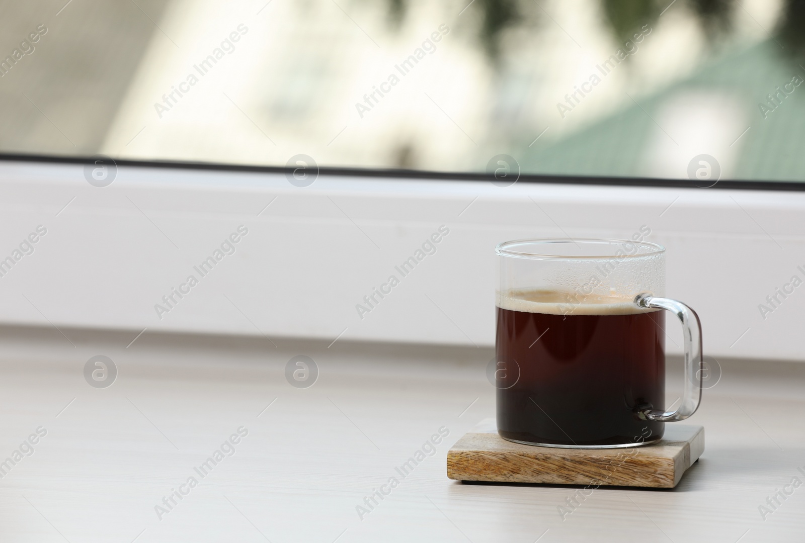 Photo of Glass cup of coffee on wooden window sill. Space for text