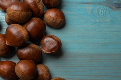 Photo of Roasted edible sweet chestnuts on light blue wooden table, flat lay. Space for text