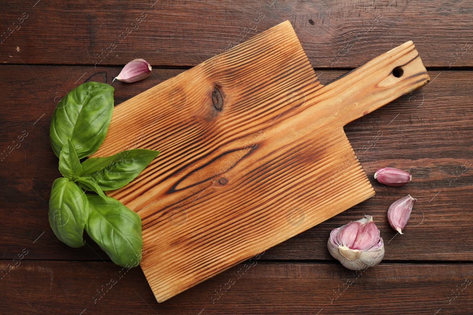 Photo of Cutting board, basil and garlic on wooden table, flat lay. Space for text