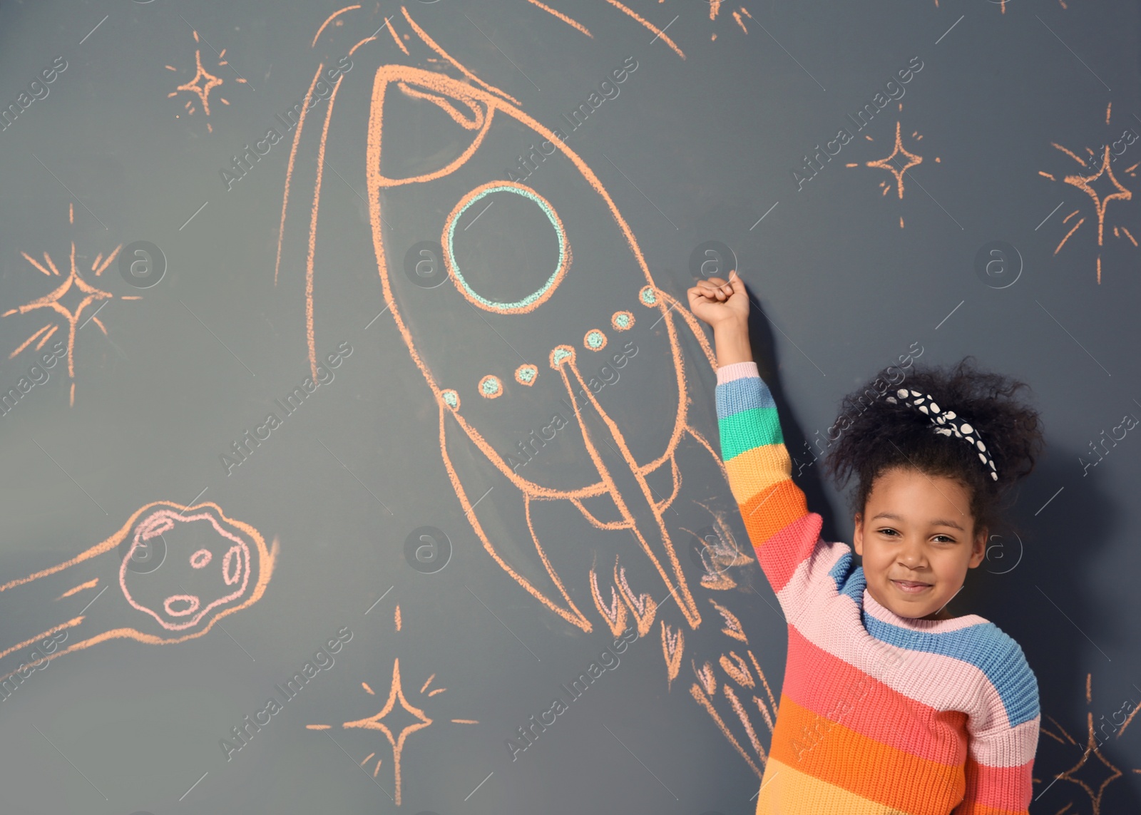 Photo of African-American child playing with chalk rocket drawing on grey background