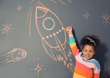 African-American child playing with chalk rocket drawing on grey background