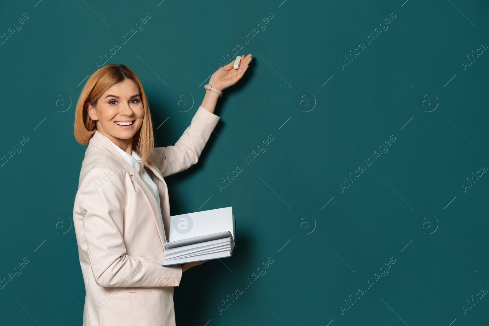 Photo of Beautiful teacher with book pointing at chalkboard, space for text