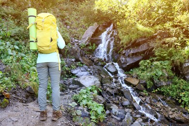 Photo of Tourist with backpack near stream in mountains, back view. Space for text