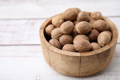 Photo of Whole nutmegs in bowl on light wooden table, closeup. Space for text