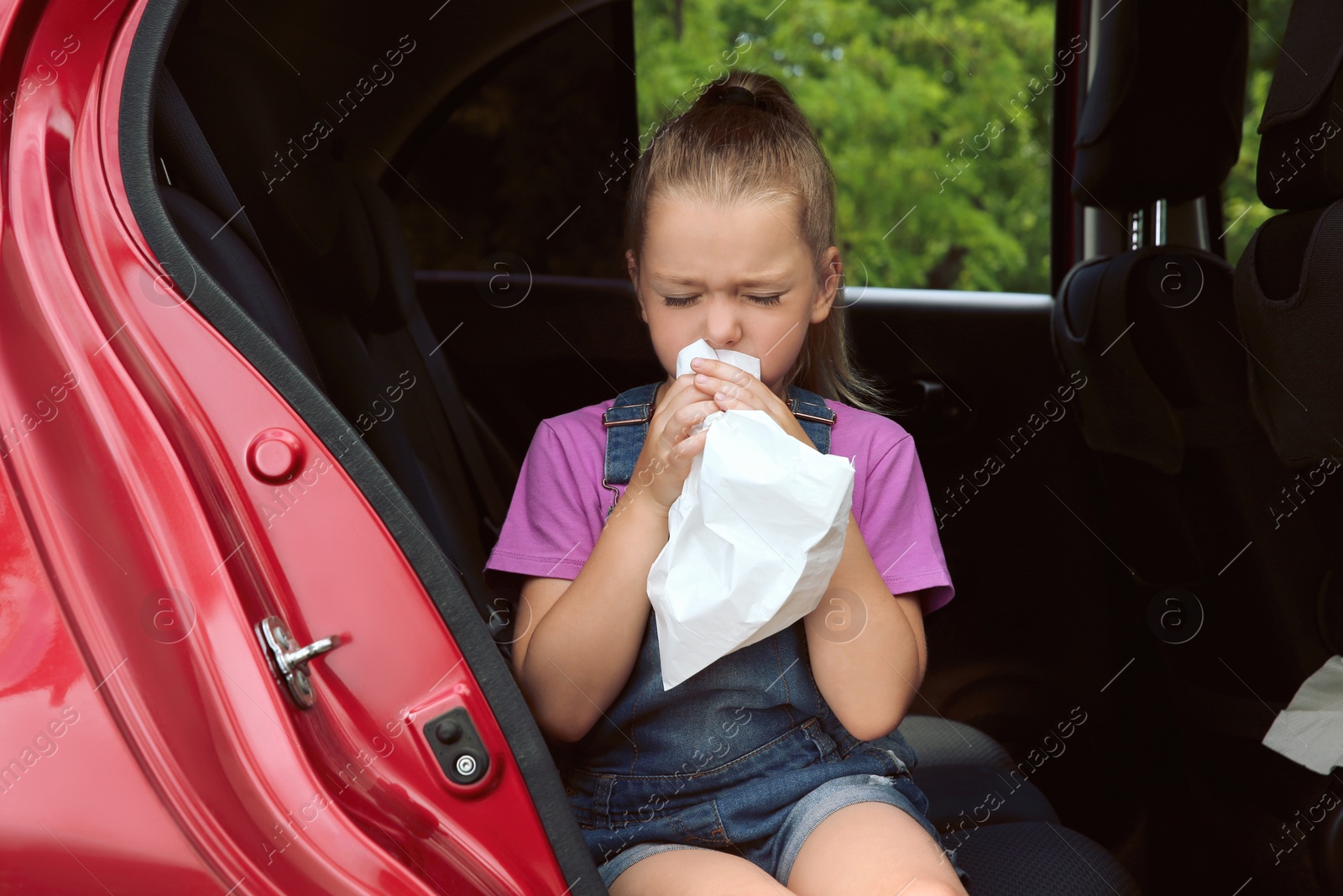 Photo of Little girl with paper bag suffering from nausea in car