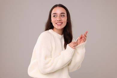 Beautiful young woman in stylish warm sweater on grey background