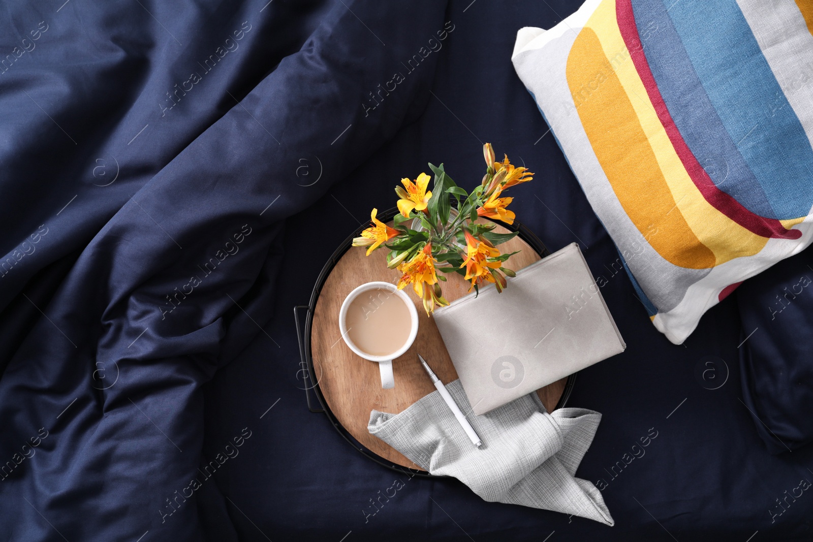 Photo of Tray with cup of coffee, notebook and flowers on fresh bed linens, top view