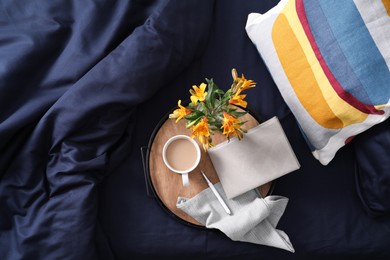 Tray with cup of coffee, notebook and flowers on fresh bed linens, top view