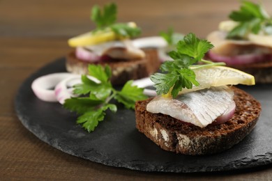Delicious sandwiches with salted herring, onion rings, parsley and lemon on wooden table, closeup
