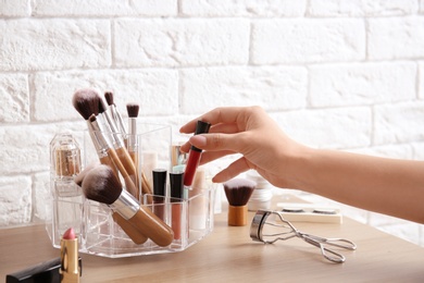 Woman taking lip gloss from organizer for makeup cosmetic products on dressing table